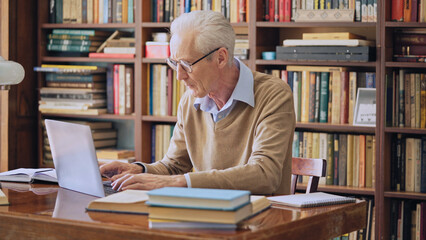 Focused senior man scientist working on laptop in the library, conducting research
