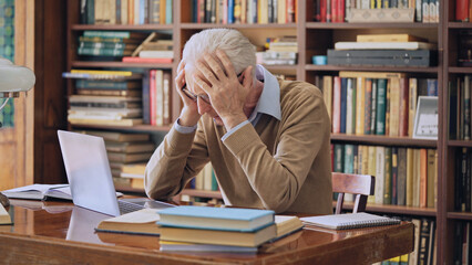 Shocked senior teacher reading e-mail on laptop, sad about project funding being declined