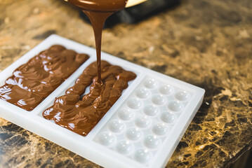Craft chocolate liquid being poured into a bar silicone mold to cool down. High quality photo