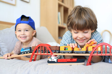 Children play a toy train on a bed in a bright room at home