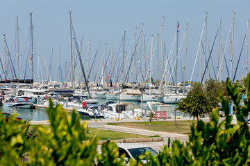 Ships on pier at sea with empty beach with clear blue water and sky. Sea port on shore with cranes and boats.