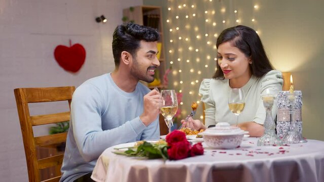 Happy couple eating dinner while talking each other during wedding anniversary at candlelight dinner - concept of romantic night, dating and engagement.