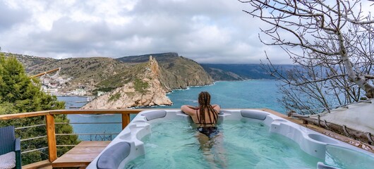 Take time for yourself. Outdoor swimsuit with mountain and sea views. A woman in a black swimsuit is relaxing in the hotel pool, admiring the view - obrazy, fototapety, plakaty