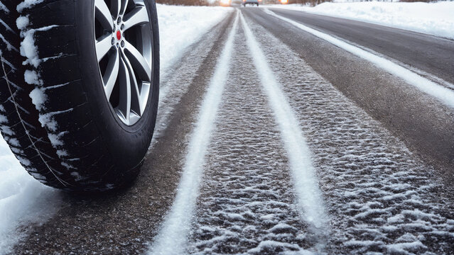 ar tire staying on long empty frozen asphalt road with snow and ice and tiry traces on it some car lights in background, generative AI