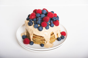 Delicious freshly cooked thick and fluffy gluten free pancakes stacked on white plate, served with cashew cream and fresh berries. Healthy food.
