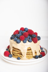 Delicious freshly cooked thick and fluffy gluten free pancakes stacked on white plate, served with cashew cream and fresh berries. Healthy food.