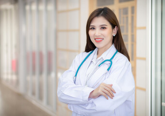 Young beautiful Asian woman doctor Standing with arms crossed happy and smile in hospital. Wearing a white robe and stethoscope.