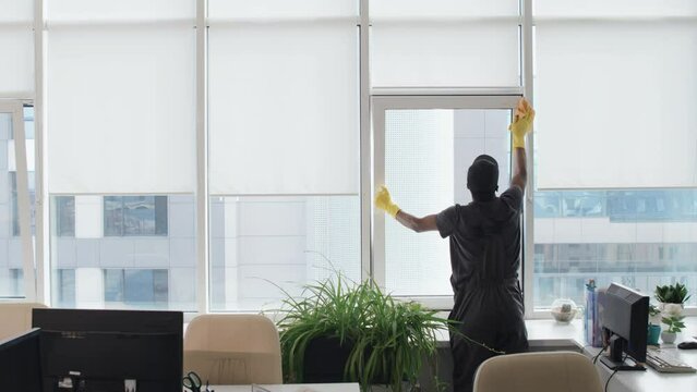 Rear view of unrecognizable man providing cleaning service in modern office wiping window with cloth