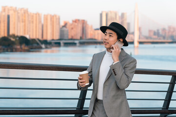 Asian businessman is making phone call near the urban river railing.