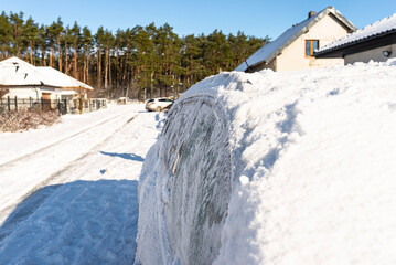 A station wagon car standing in front of a panel fence covered with ice and snow.