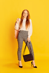 Young charming girl with red hair wearing office style clothes posing over yellow background. Concept of youth, student college life, business and education.