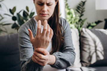Selective focus of tired young pregnant female expecting baby suffering pain on hand and fingers sit alone on couch at home, arthritis inflammation, future mother massaging wrists. Rheumatism concept