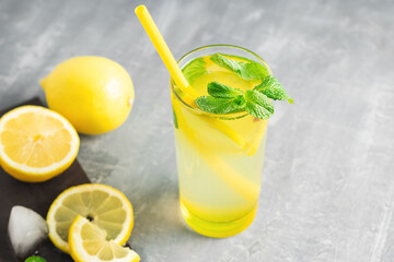 Lemonade drink or mojito cocktail in a glass with straw, lemon fruit and mint leaves, refreshing summer beverage