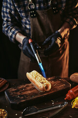 A guy in an apron and gloves sprinkles cheese on a hot dog. Hot dog cooking. Creating classic fast food.