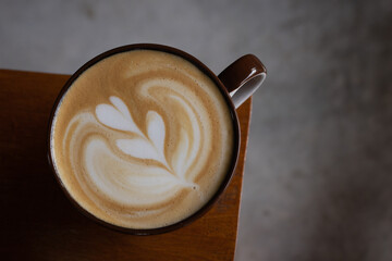 Side view of hot latte coffee with latte art in a ceramic cup on wood table.