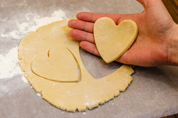 A man's hand holding homemade heart shaped cookie from ginger raw dough, homemade pastry for Valentine day