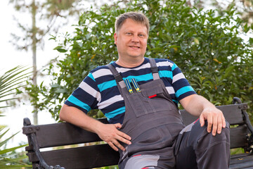 A man work clothes is resting sitting on bench.