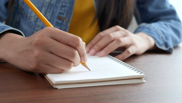 4K: cropped short, Hands of Young woman holding pen making notes in diary, close up view. 