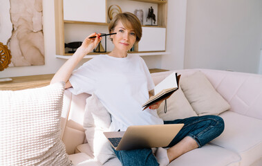 Positive woman with diary in hands working on netbook