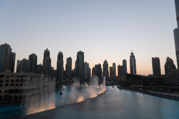 Obraz premium Dubai singing fountains at night lake view between skyscrapers. City skyline in dusk modern architecture in UAE capital downtown.