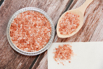 Small granules of natural Himalayan salt in a decorative plate and in a wooden spoon on a wooden background