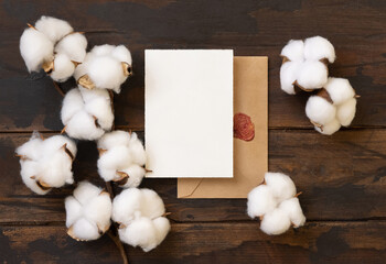 Blank card and envelope with cotton flowers top view on dark brown wood, wedding mockup