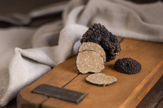 Whole and sliced black truffles mushroom on wooden board on dark brown table, close up