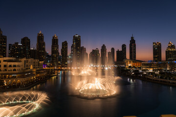 Fototapeta na wymiar Dubai singing fountains at night lake view between skyscrapers. City skyline in dusk modern architecture in UAE capital downtown.