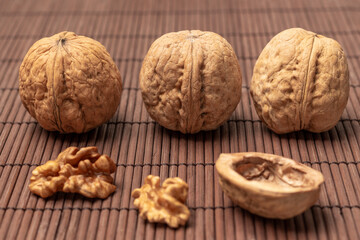 Three whole walnuts, walnut kernel and walnut shell on napkin of thin wooden sticks.