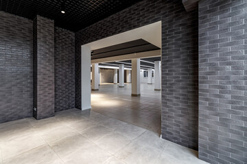 A large empty room with ceramic tiles on the floor, a black ceiling with lighting and columns propagating the ceiling