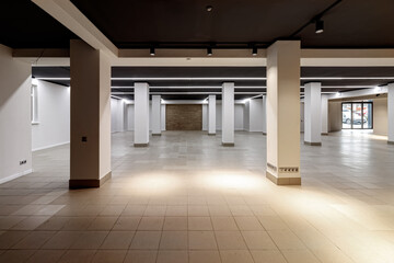 A large empty room with ceramic tiles on the floor, a black ceiling with lighting and columns propagating the ceiling