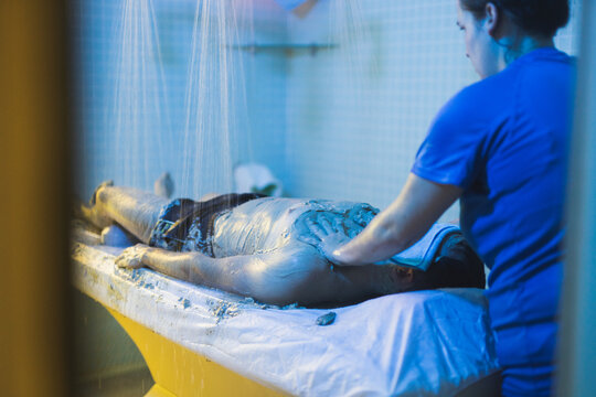 Professional therapist applying mud on client in spa center