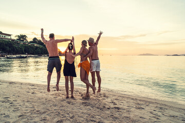 Group of happy friends enjoying beautiful sunset at the tropical beach, jumping and having fun together. Travelers.