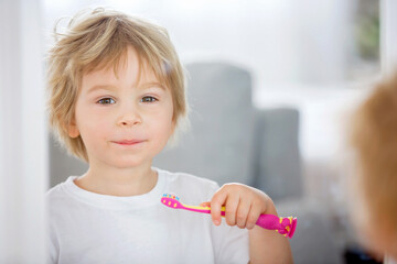 Cute toddler child, blond boy, brushing his teeth at home