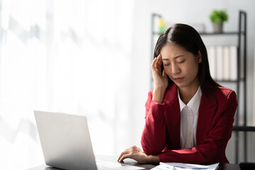 Tired Asian business woman with headache at office, feeling sick at work ater a busy day.