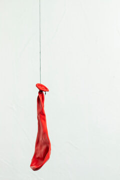Deflated red balloon. Hanging on a black thread.