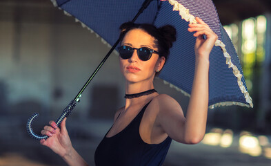 Goth ballerina holding a parasol and wearing sunglasses posing in an abandoned building	