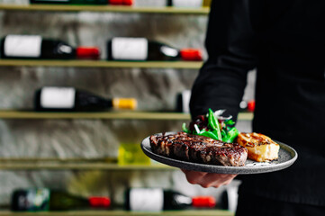 Young handsome chef in black uniform hold in his hands ready beef steak  ribeye meat 