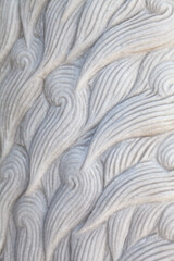 Animal fur curly waves pattern carved in stone close-up. White sculpture repetitive detail background