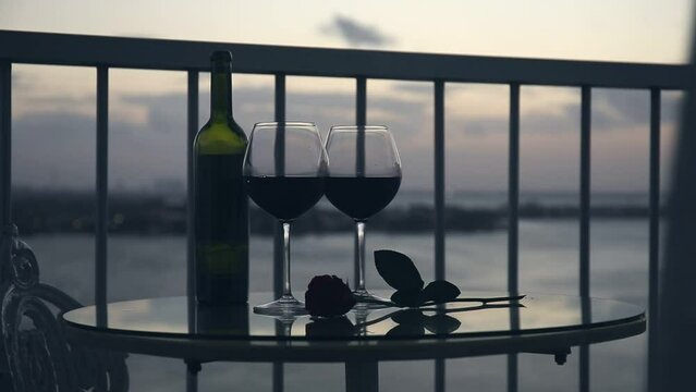 Pouring red wine in to glasses on balcony overlooking at sunset. Closeup