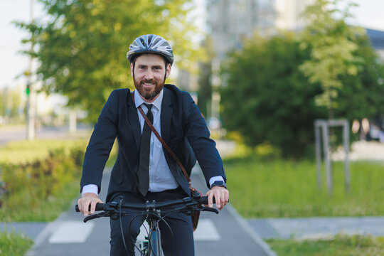 Happy bearded worker looking at camera, while driving bicycle outdoors.