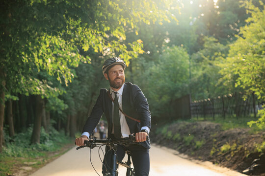 Handsome manager in smart casual riding bike through park area.