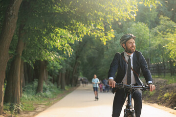 Cheerful male entrepreneur riding on bicycle after workday in city park.