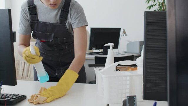 Slowmo tilt up of young female cleaning service worker wiping desk in modern office using detergent and cloth