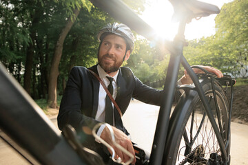 Smiling businessman squatting down for checking bike wheel in park.