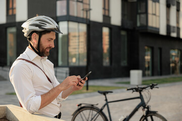 Smiling bearded man in helmet with bike telephoning on street.