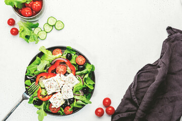 Vegetable greek salad with feta cheese, olives, tomatoes, paprika, cucumber and red onion, healthy mediterranean food, low calories eating. White stone background, top view