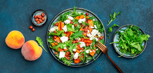 Delicious grilled peach salad  with cheese, hazelnuts and arugula on blue background, top view banner