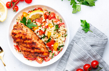 Grilled chicken breast fillet with tabbouleh salad with bulgur, tomato and parsley with lemon dressing, white table background, top view