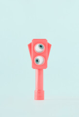 Pink semaphore with two eyes looking around on isolated pastel blue background. Minimal creative abstract surreal aesthetic concept of surveillance, observation or monitoring. Idea of urban control.